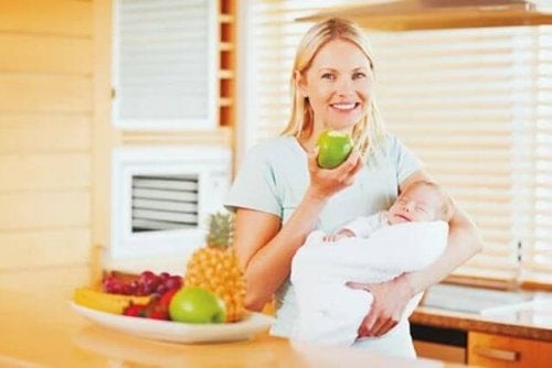 A woman eting an apple while holding her newborn.