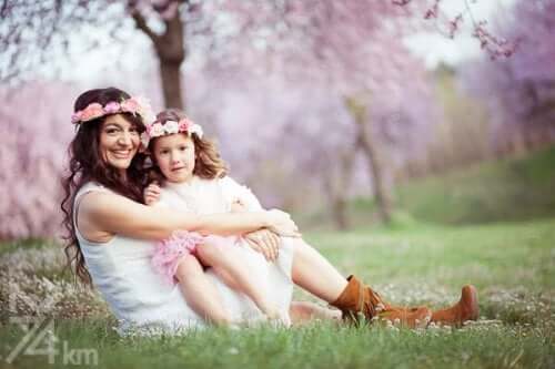 A mother and her young dauther sitting in a field and wearing flower crowns.