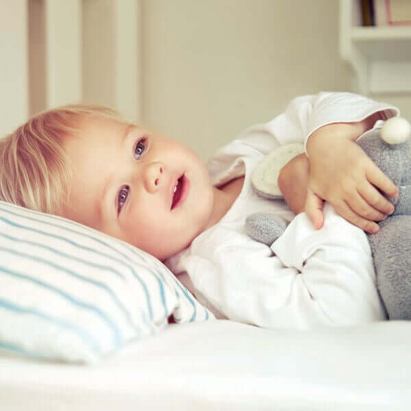 A happy toddler lying in his own bed.