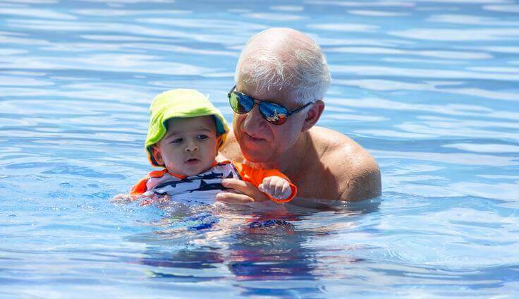 En bestefar i bassenget med bestebarnet sitt.