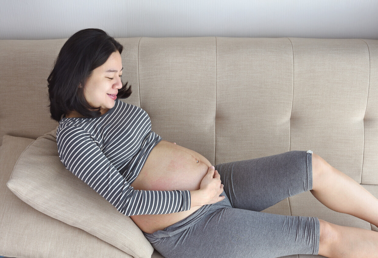 En gravid kvinna ligger med ryggstöd på en soffa.