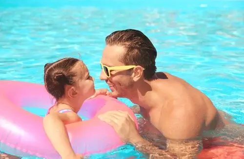 A father and daughter with their faces close to one another smiling in a pool.