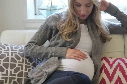 A mother looking down at her pregnant belly.