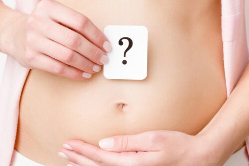 A woman holding a paper with a question mark on it over her bare abdomen.