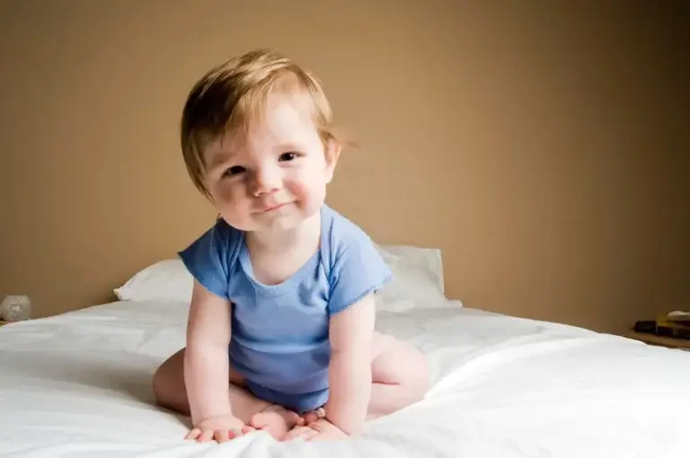 En liten gutt sitter oppe og smiler.