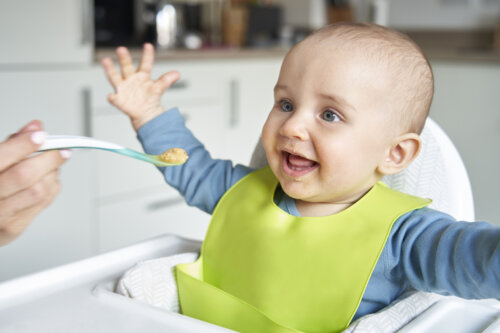 A person offering a happy baby pureed food on a spoon.