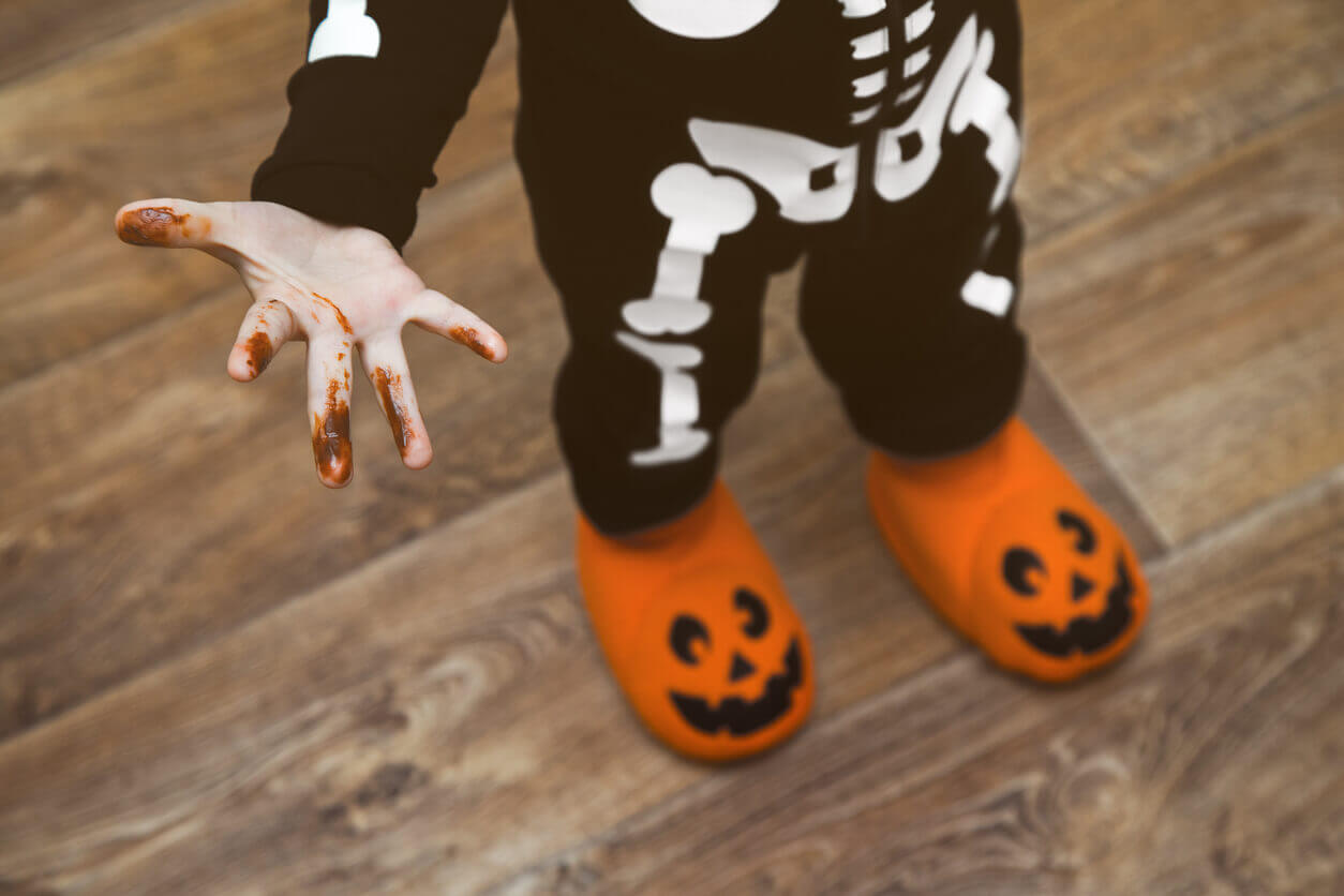 A little boy wearing a halloween costume with melted chocolate on his fingers.