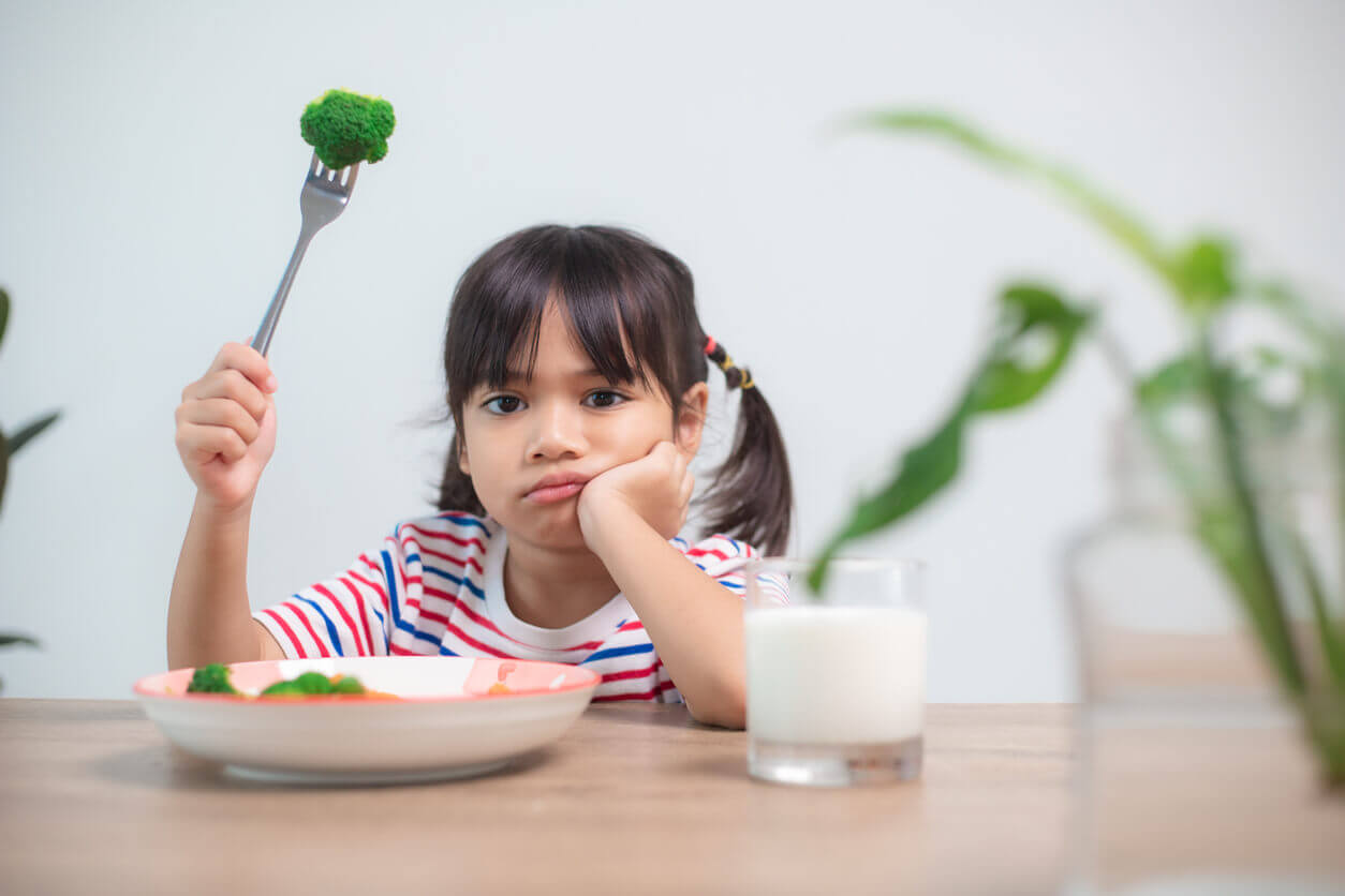 A child looking uninterested in eating her brocolli.