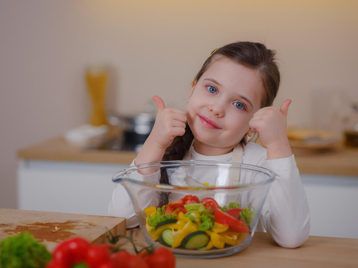A young girl giving two thumbs up to a salad.