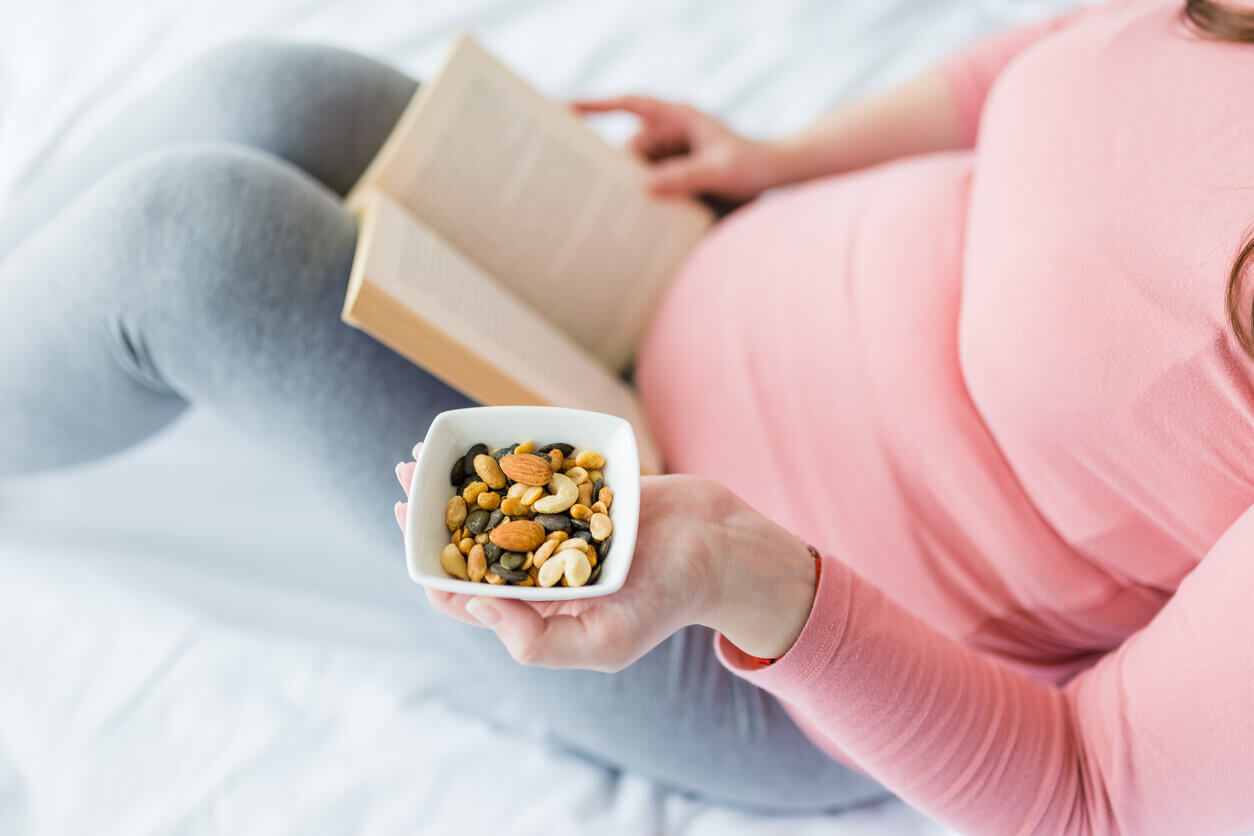 A pregnant woman reading and eating nut mix.