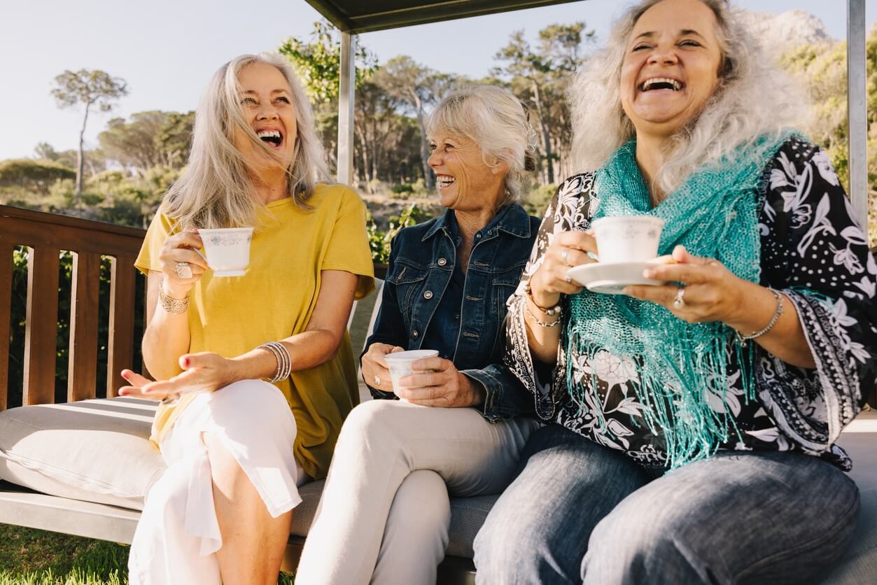 Three older women drinking tea and laughing.
