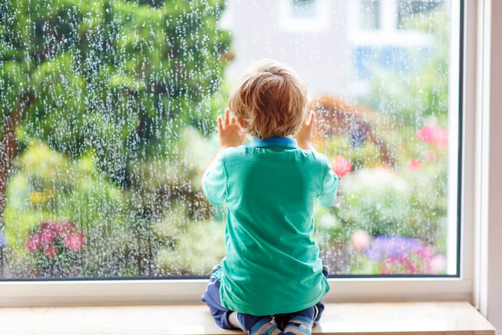 A boy looking out a window on a rainy day.