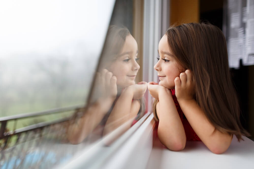 En ung flicka tittar ut genom ett fönster.
