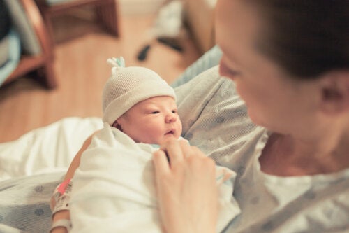 A mother looking down at her newborn baby who's swaddled in a blanket and wearing a knit cap.