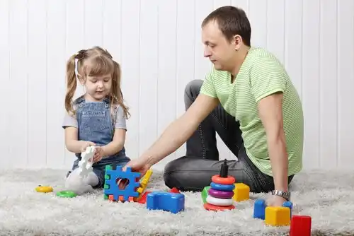 A man sitting on the floor with a little girl who's playing with toys.
