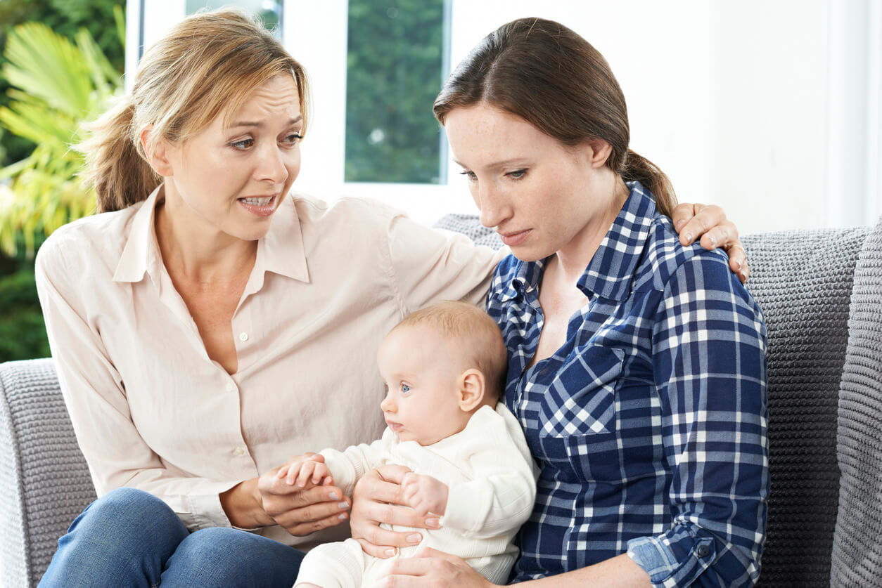A woman puttin her arm on the shoulder of a new mother who looks sad.