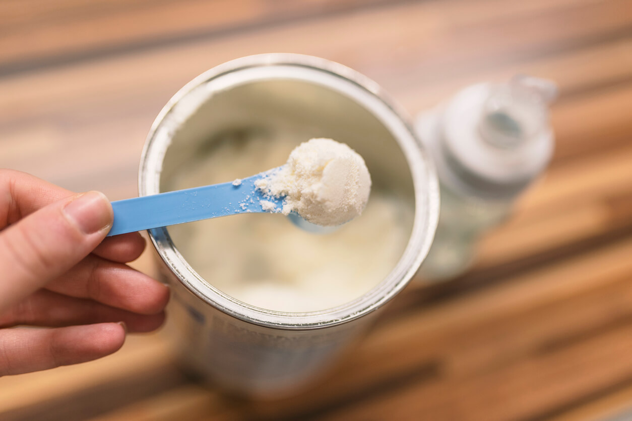 A close-up of a woman's hand scooping baby formula from a canister.