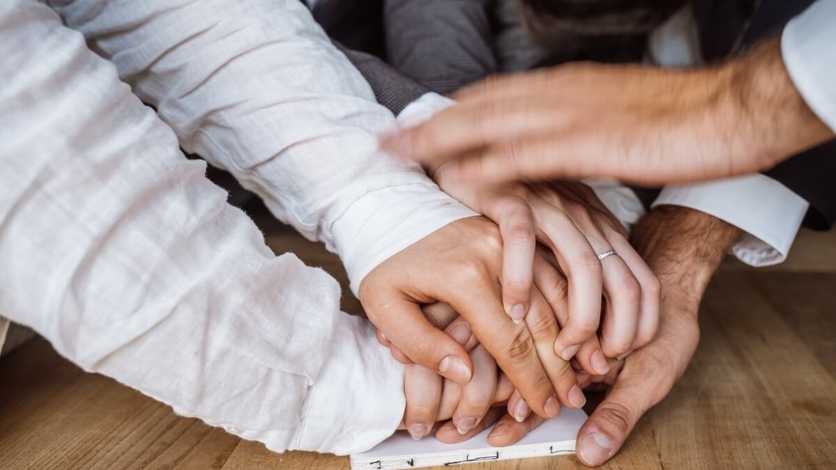 Several people's hands piled on top of one another in a supportive gester.