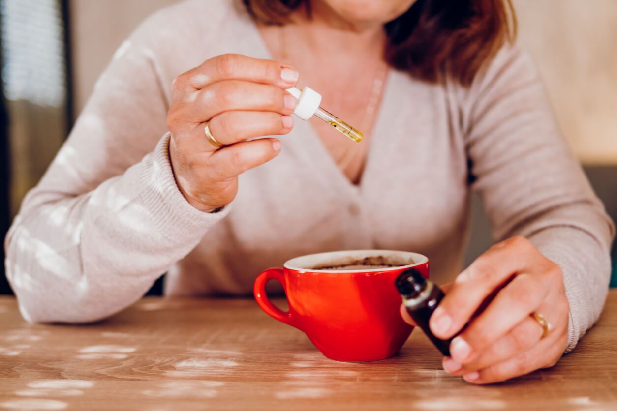A woman adding CBD drops to her coffee.